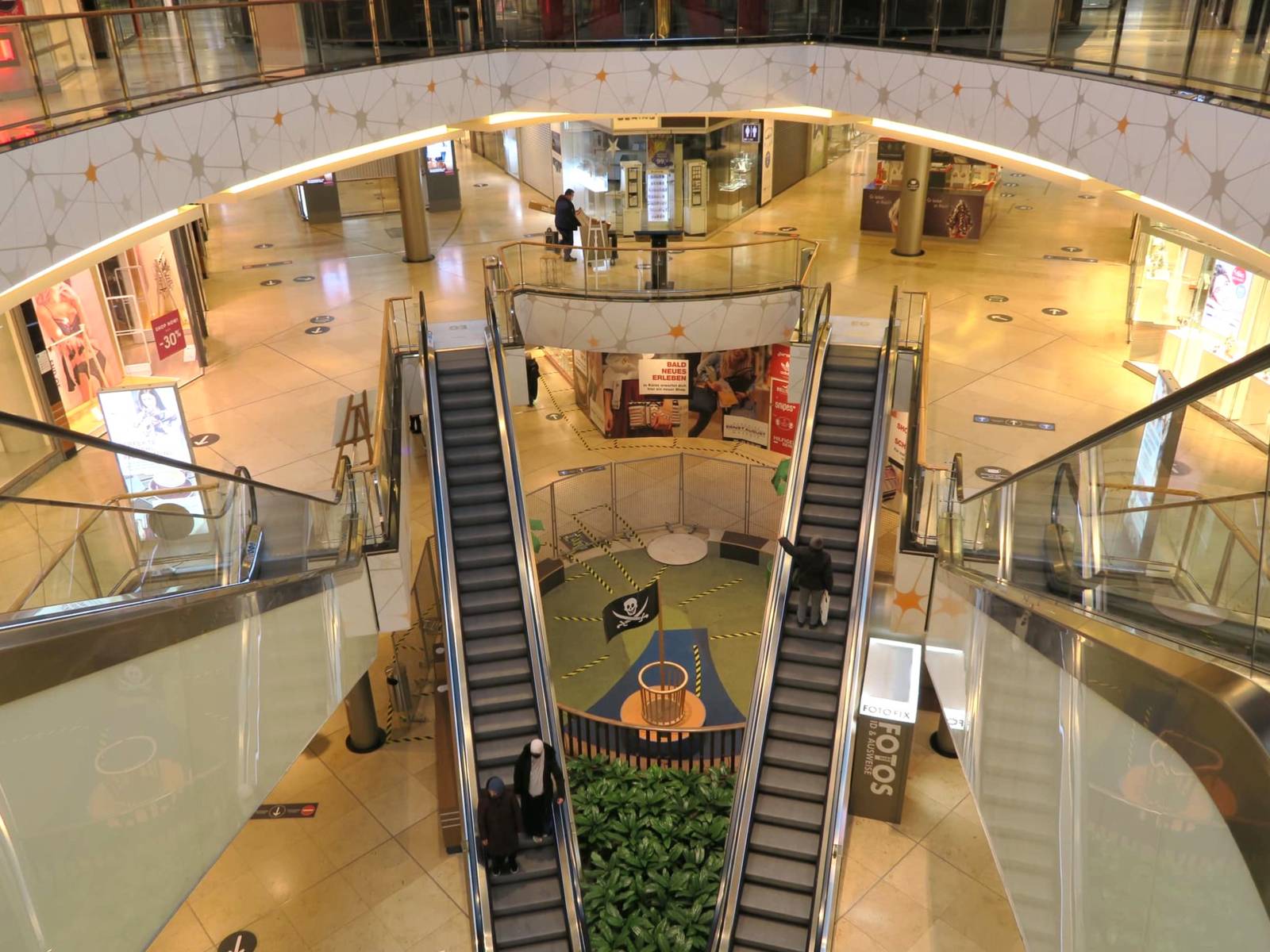 Mehrgeschossige Einkaufsgalerie mit Rolltreppen und nur vereinzelten Besuchern.